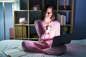 Young hispanic woman using computer laptop on the bed showing middle finger, impolite and rude fuck off expression