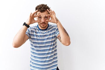 Handsome young man standing over isolated background trying to open eyes with fingers, sleepy and tired for morning fatigue