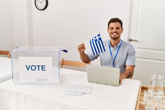 Young hispanic man smiling confident holding greece flag working at electoral college
