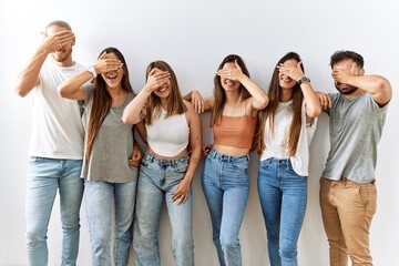 Obraz premium Group of young friends standing together over isolated background smiling and laughing with hand on face covering eyes for surprise. blind concept.