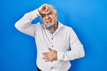 Middle age man with grey hair standing over blue background touching forehead for illness and fever, flu and cold, virus sick