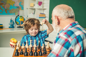 Family relationship between grandfather and grandson. Grandpa teaching school boy playing chess.