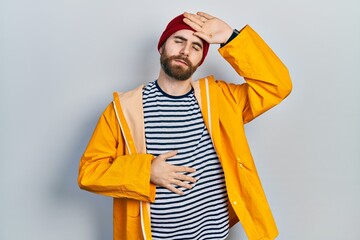 Caucasian man with beard wearing yellow raincoat touching forehead for illness and fever, flu and...