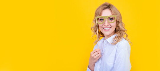 positive woman with funny party glasses on yellow background. Woman isolated face portrait, banner with mock up copy space.