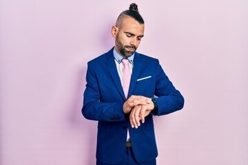 Young hispanic man wearing business suit and tie checking the time on wrist watch, relaxed and confident