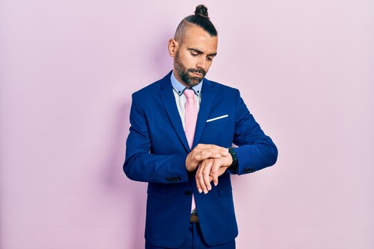 Young hispanic man wearing business suit and tie checking the time on wrist watch, relaxed and confident