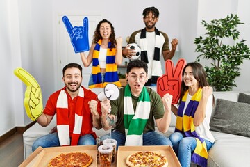 Group of young people wearing team scarf cheering football game screaming proud, celebrating victory and success very excited with raised arms