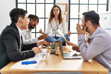 Businesswoman enjoys meditating during meeting. Sitting on desk near arguing partners at the office.