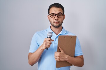 Hispanic man holding reporter microphone and clipboard depressed and worry for distress, crying...