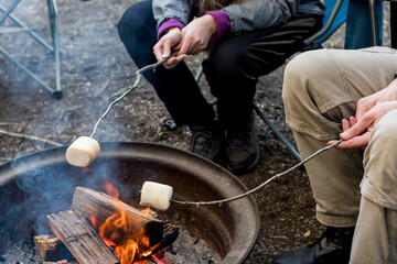 People roasting large marshmallows on a stick over the campfire firepit. Camping family fun