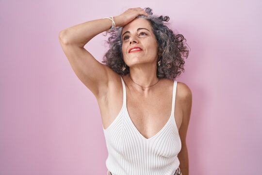 Middle age woman with grey hair standing over pink background smiling confident touching hair with hand up gesture, posing attractive and fashionable