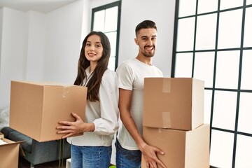 Young hispanic couple smiling happy holding cardboard boxes moving at new home.