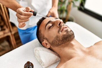 Obraz premium Two hispanic men therapist and patient having facial treatment using serum at beauty center
