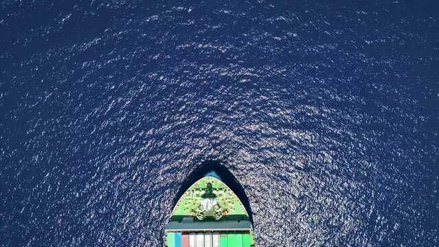 Aerial top down view of a loaded cargo container ship traveling with speed over blue ocean