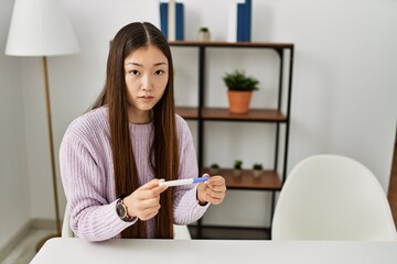 Young chinese girl holding pregnancy test sitting on the table at home.