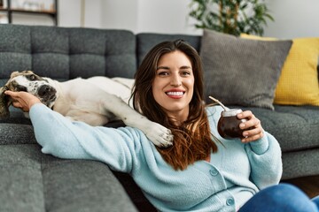 Young woman hugging dog drinking mate infusion at home
