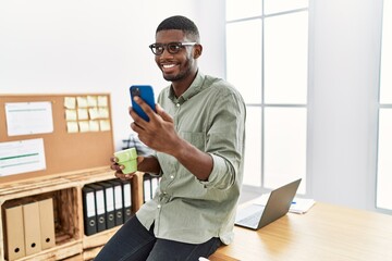 Young african american man using smartphone drinking coffee at office