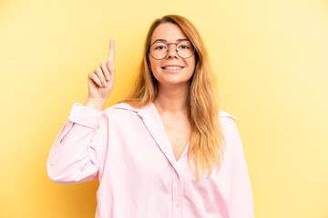 blonde pretty woman smiling cheerfully and happily, pointing upwards with one hand to copy space