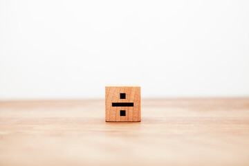 ÷の文字。割る。割り算。除法。木製ブロックに書かれている。黒い文字。木製テーブルの背景。