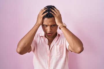 Young hispanic man standing over pink background suffering from headache desperate and stressed because pain and migraine. hands on head.