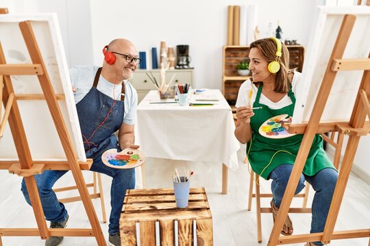 Middle age hispanic painter couple smiling happy using headphones and painting at art studio.