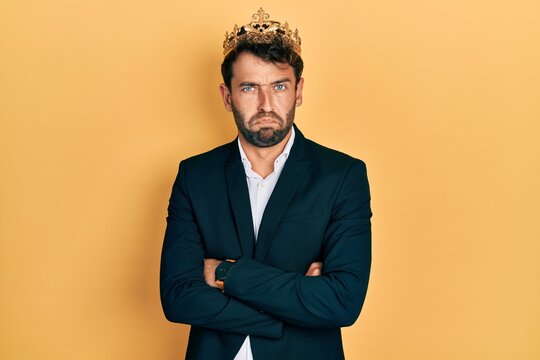Handsome man with beard wearing business suit with arms crossed gesture and king crown depressed and worry for distress, crying angry and afraid. sad expression.
