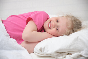 Obraz na płótnie Canvas blond little girl lies on the bed with her hand under her cheek