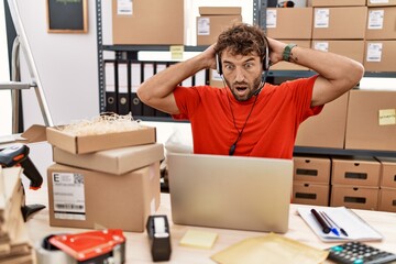 Young hispanic call center agent man working at warehouse crazy and scared with hands on head,...