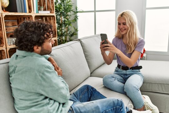 Young woman making picture of her boyfriend using smartphone at home