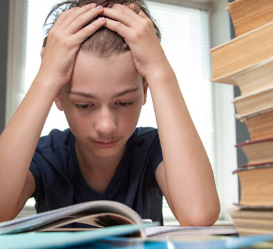 Portrait of upset schoolboy looking at textbook with homework