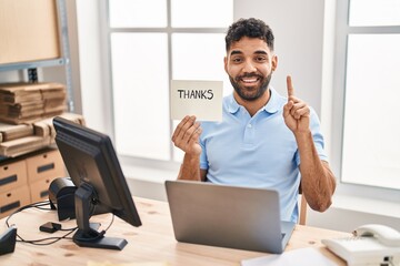 Hispanic man with beard working at the office with laptop holding thanks banner smiling with an...