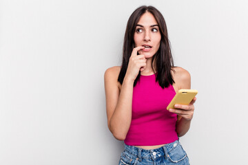 Young caucasian woman holding mobile phone isolated on white background relaxed thinking about something looking at a copy space.