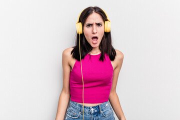 Young caucasian woman listening to music isolated on white background screaming very angry and aggressive.