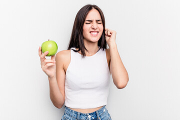 Young caucasian woman holding an apple isolated on white background covering ears with hands.