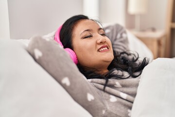 Young chinese woman listening to music lying on bed at bedroom