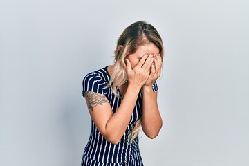 Beautiful young blonde woman wearing casual striped dress with sad expression covering face with hands while crying. depression concept.