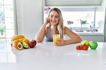Young woman smiling confident holding orange juice at kitchen