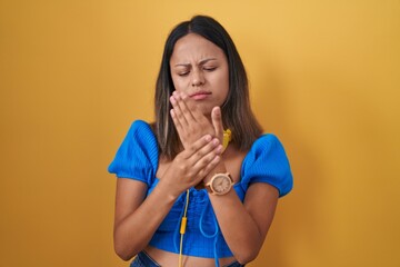 Hispanic young woman standing over yellow background suffering pain on hands and fingers, arthritis...
