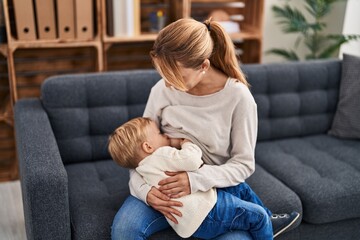 Mother and son breastfeeding kid sitting on sofa at home