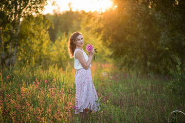 Fototapeta na wymiar Beautiful happy young girl with peonies in nature outdoors in the sun. Beautiful woman in a field with flowers in a long skirt