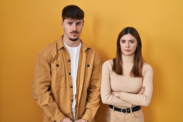 Young hispanic couple standing over yellow background skeptic and nervous, frowning upset because of problem. negative person.