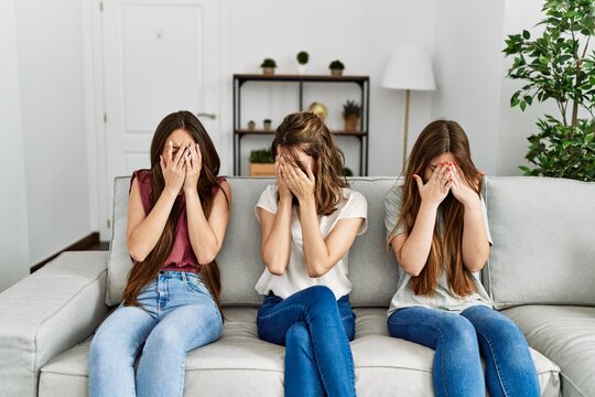 Group Of Three Hispanic Girls Sitting On The Sofa At Home With Sad Expression Covering Face With Hands While Crying. Depression Concept.