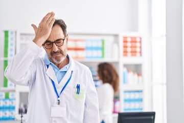 Middle age hispanic man working at pharmacy drugstore surprised with hand on head for mistake,...