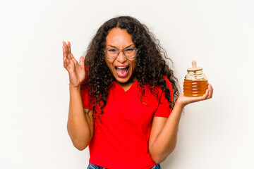 Young hispanic woman holding honey jar isolated on white background receiving a pleasant surprise,...