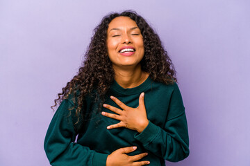 Young hispanic woman isolated on purple background laughs happily and has fun keeping hands on...
