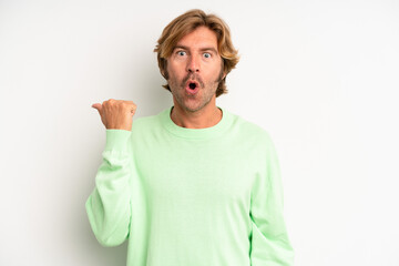 blond adult man looking astonished in disbelief, pointing at object on the side and saying wow,...