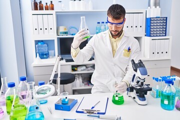 Fototapeta premium Young hispanic man wearing scientist uniform measuring liquid at laboratory