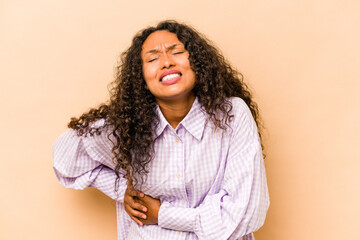 Young hispanic woman isolated on beige background having a liver pain, stomach ache.
