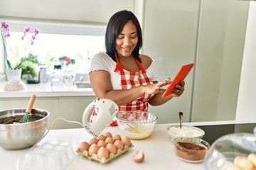 Obraz na płótnie Canvas Hispanic brunette woman preparing cake looking at online recipe at the kitchen