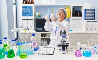 Fototapeta premium Middle age woman wearing scientist uniform looking test tubes at laboratory